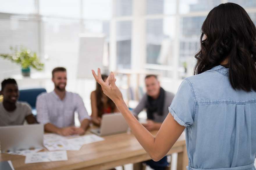 Woman standing up presenting to 4 people at a desk